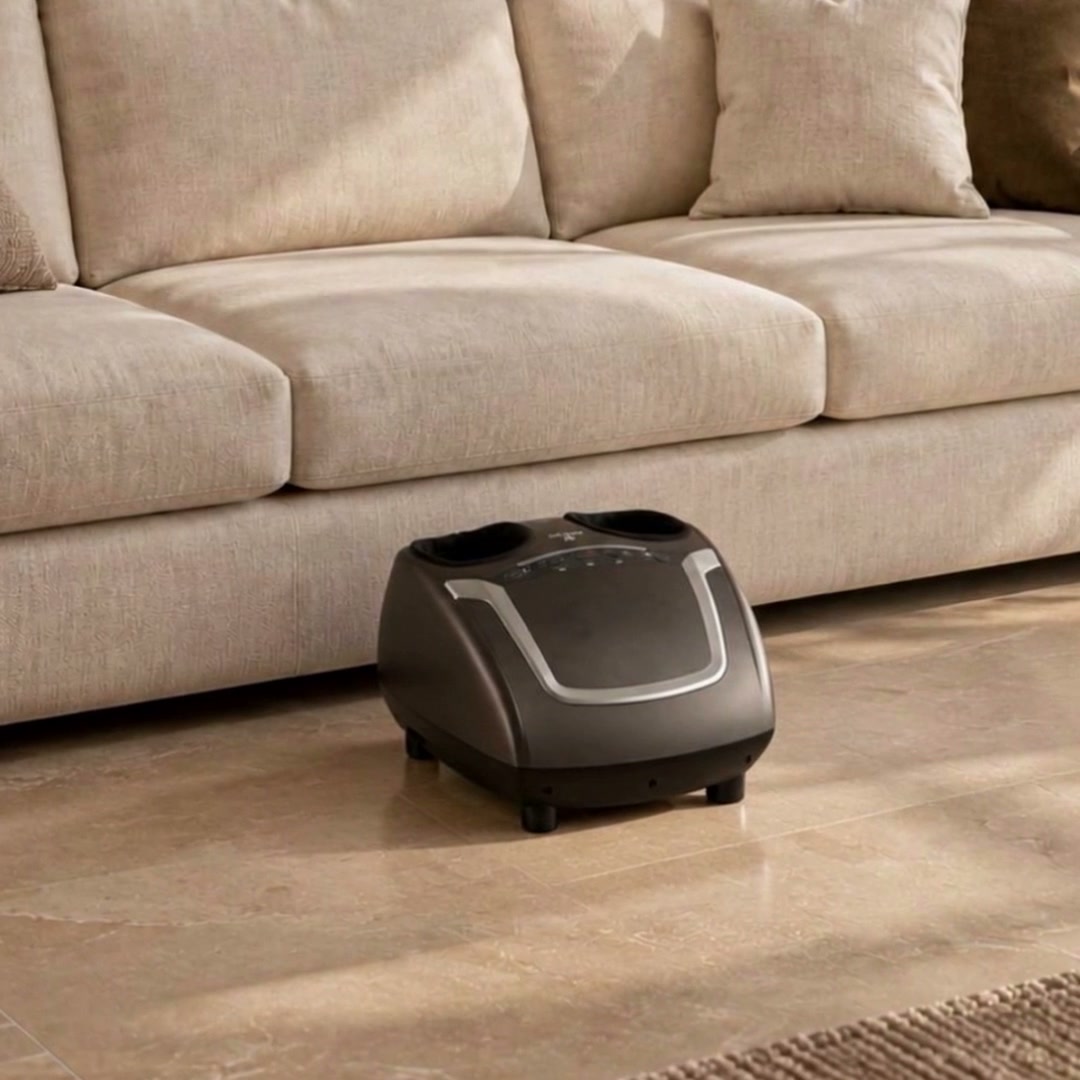 Compact Zarifa Z-Smart Foot Massager in front of an ivory sofa in a warm luxury living room, with close-ups of the five controls and silver trim.